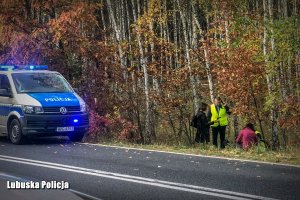 radiowóz na drodze przy lesie, policjanci oglądają rower