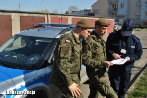 żołnierze i policjantka przy radiowozie. Policjantka tłumaczy żołnierzom wpisy w dokumencie który trzymają w dłoni