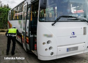 Policjant sprawdzający stan ogumienia w autobusie