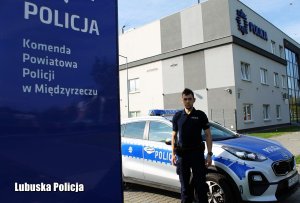 dzielnicowy Jakub Pendrak stojący przy radiowozie oznakowanym zaparkowanym przy Komendzie Powiatowej Policji w Międzyrzeczu
