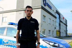 dzielnicowy Jakub Pendrak stojący przy radiowozie zlokalizowanym przy siedzibie Komendy Powiatowej Policji w Międzyrzeczu