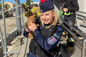Policjantka stojąca przodem trzymająca małego rudego rudego kotka, policjantka uśmiecha się.