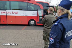 policjantka i żołnierze czekający w kolejce przed autokarem poboru krwi