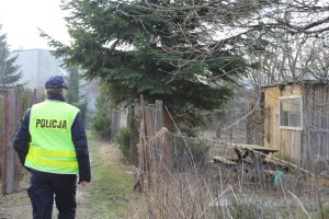 policjant stojący tyłem patrzący na altanę. Panują ponure warunki atmosferyczne.