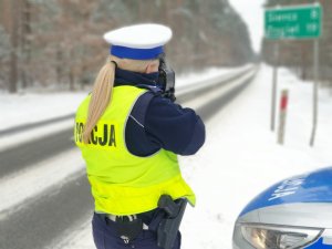 Policjanta z Wydziału Ruchu drogowego stojąca tyłem do zdjęcia wykonująca pomiar... w tle zaśnieżona droga