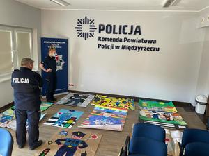 Policjanci będący w jury w trakcie przyznawania punktacji za przesłane prace. Na zdjęciu widać policjanta stojącego tyłem oraz policjantkę pochylających się nad nadesłanymi pracami.