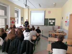 Policjantka stojąca przodem do uczniów klas podstawowych w trakcie pogadanki n a temat odpowiedzialności karnej nieletnich. Zajęcia w klasie szkoły średniej