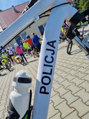 rama roweru policyjnego z napisem policja w tle dzieci na rowerach ubrane w kamizelki odblaskowe