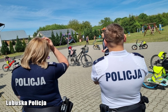 policjanci stojący tyłem w tle plac z rowerami
