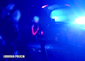 zdjęcie zrobione w trakcie interwencji nocą. Światło radiowozu rozmazuje część zdjęcia ma którym widać część pojazdu oraz sylwetki osób zaginionych