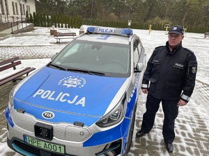 policjant stojący przy oznakowanym radiowozie- aura zimowa