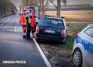 pojazd stojący na poboczu na drugim planie pojazd karetki pogotowia oraz stojący policjant i ratownicy medyczni