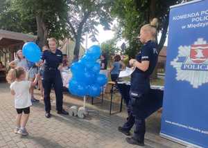 Policjanci przy stoisku promocyjnym trzymają balony