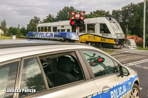 na pierwszym planie radiowóz w drugim przejeżdżający pociąg i przejazd kolejowy