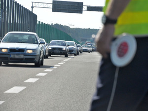 tarcza do zatrzymywania pojazdów w dłoni policjanta w tle sznur pojazdów osobowych na drodze ekspresowej