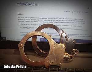 zdjęcie przedstawia kajdanki oparte o włączony ekran komputera wyświetlający kodeks karny na artykule dotyczącym oszustw