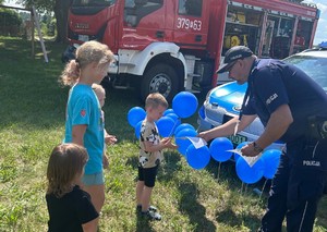 Policjant wręcza niebieski balon dziecku