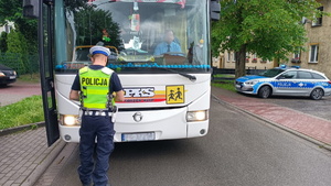 policjant wydziału ruchu drogowego stoi obrócony tyłem przy autobusie szkolnym koloru białego