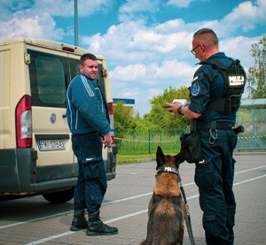 policjant, pozarant oraz policyjny pies stoją przy kremowym busie