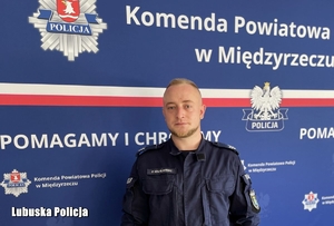 sierżant sztabowy Patryk Maciejewski- wizerunek policjanta stojącego na tle ścianki koloru granatowego z logo i napisem Policja