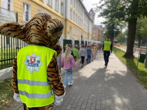 lupo, dzieci i policjantki idą po chodniku. Zdjęcie zrobione z tyłu