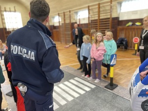 policjant stojący tyłem. Dzieci ćwiczą na symulatorze przejścia dla pieszych