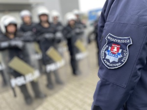 policjant w trakcie szkolenie uczniów pracy w pododdziałach zwartych , zbliżenie na herb Komendy Powiatowej Policji w Międzyrzeczu