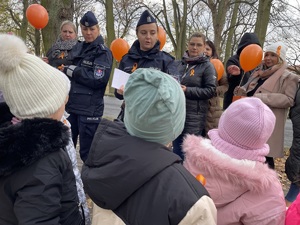 policjanci i pracownicy Ośrodka Pomocy Społecznej rozdają pomarańczowe wstążki dla dzieci