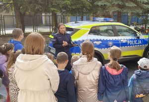 policjantka stojąca przy radiowozie w trakcie pogadanki z dziećmi i ich opiekunami