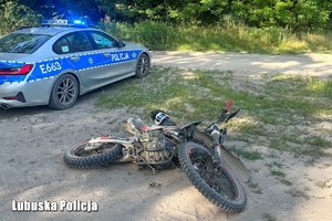 motocykl typu cross leży na ziemi, obok radiowóz z włączonymi sygnałami świetlnymi
