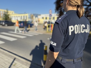 policjantka stoi przy przejściu dla pieszych gdzie przechodzą ludzie
