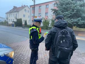 na zdjęciu widzimy policjanta z wydziału ruchu drogowego, ubranego w białą czapkę i żółtą kamizelkę odblaskową. Policjant przeprowadza kontrolę trzeźwości osoby poruszającej się rowerem.