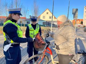 na zdjęciu rowerzysta i policjantki, które umieszczają odblask na rowerze